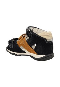 Scarpa in suede nera e marrone con cinturini in velcro, tacco beige perforato, suola intermedia bianca e suola esterna in gomma nera texturizzata.