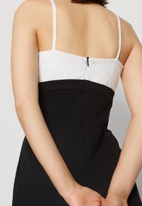 Zwart-witte jurk met een getailleerd silhouet, spaghettibandjes, ritssluiting aan de achterkant en gladde stof met een gestructureerd ontwerp.