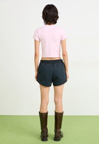 Light pink cropped short-sleeve shirt paired with black athletic shorts featuring a drawstring waistband and brown accents. Brown knee-high boots.