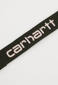 Juodas audinys diržas su žodžiu "carhartt" išsiuvinėtu šviesiai rožine spalva. Audinys yra textured ir tvirtas.
