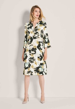 Blumenkleid mit einem Farbschema in Grün, Weiß und Schwarz; verfügt über einen V-Ausschnitt und dreiviertellange Glockenärmel; knieumspielendes Design.