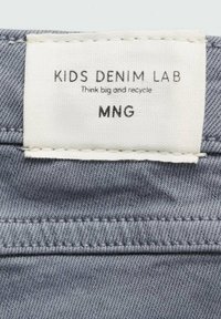 Dětská denimová látková etiketa v světle modro-šedé barvě, bílý obdélníkový štítek se nápisem "KIDS DENIM LAB," poznámky o recyklaci a značka "MNG."