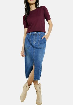Bordeaux kortemouwtop gedragen met een knielange, lichtblauwe denimrok met een voorknof en twee zakken; gecombineerd met tan cowboylaarzen.
