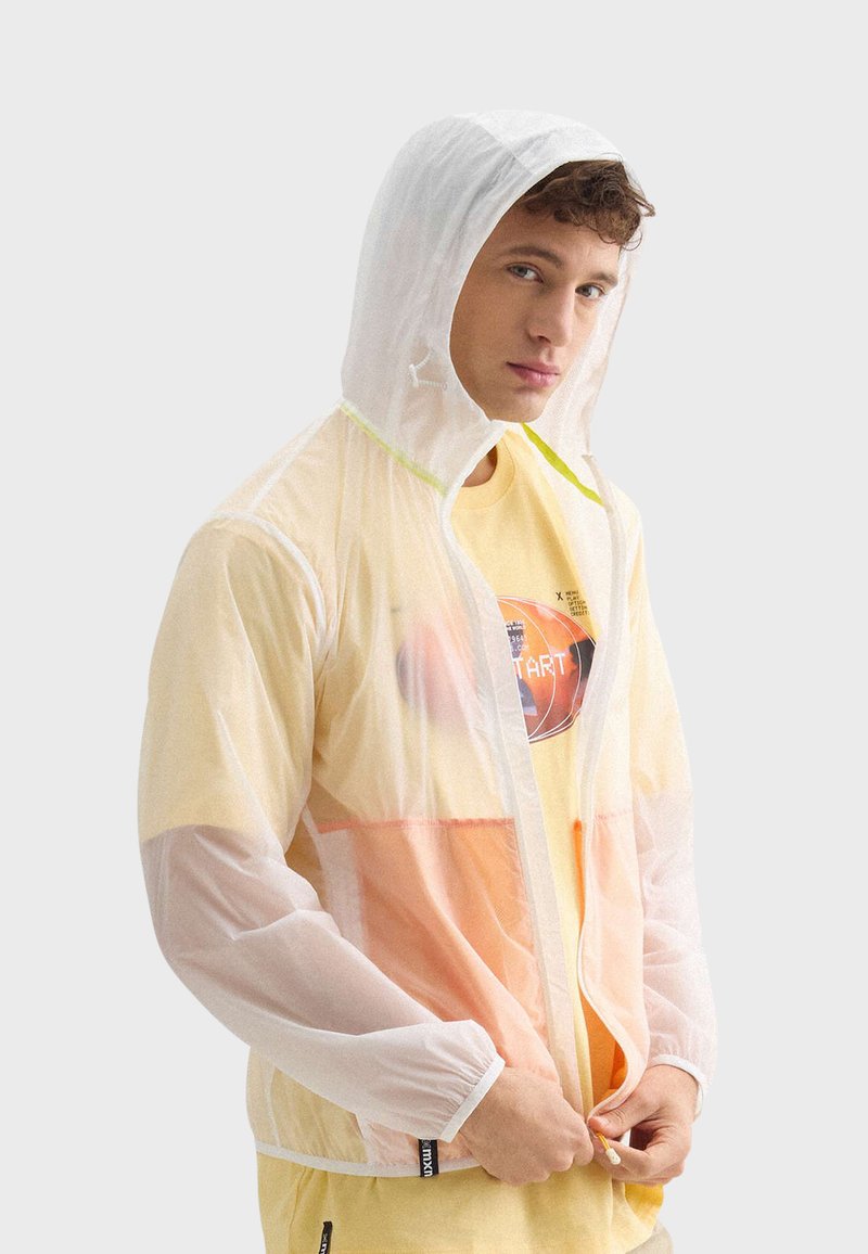 Veste blanche transparente avec une capuche ajustable, dotée d'accents vert fluo et d'un design superposé dans des teintes orange et jaune.