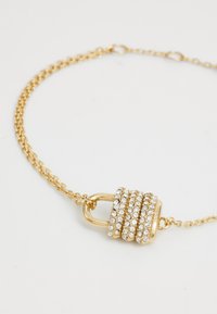 Collana in oro con ciondolo a forma di lucchetto decorato con più file di strass trasparenti, che riflettono la luce e aggiungono texture.