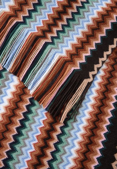 Gros plan d'un tissu tricoté multicolore avec des motifs en zigzag et des bords à franges assortis dans des tons marron, vert, bleu, noir et beige.