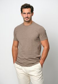 T-shirt marrone a maniche corte realizzato in tessuto leggero, con collo rotondo e design aderente, abbinato a pantaloni color crema.