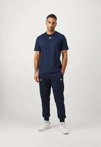 Granatowy sportowy strój składający się z koszulki z krótkim rękawem i zwężanych spodni dresowych, oba z subtelnymi akcentami z logo, zestawiony z białymi trampkami.