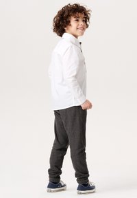 Vit långärmad skjorta med krage, matchad med mörka, strukturerade, avsmalnande byxor. Blå sneakers har vita detaljer och snören.