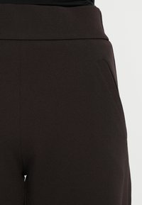 Καφέ παντελόνια με ομαλή υφή, που διαθέτουν φαρδιά μέση και πλαϊνές τσέπες, με κομψή γραμμή και μινιμαλιστικό σχέδιο.