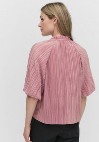 Vaaleanpunainen poimutettu pusero lyhyillä hihoilla ja korkealla kauluksella. Takana nappisuljenta ja teksturoitu kangasmateriaali.