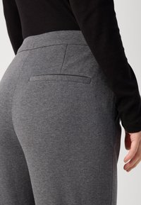 Grå, myke stoffbukser med slim fit og detaljer på baklommen. Livlinjen er elastisk for komfort og enkel bruk.