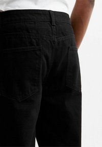 Jeans in denim nero con un taglio classico, design a cinque tasche e cuciture visibili, che mostrano una texture liscia e un tessuto resistente.