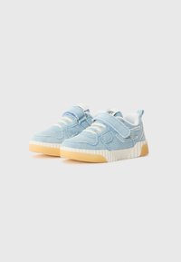 Baskets en denim bleu avec accents blancs, bandoulières Velcro et semelles texturées. Elles présentent une semelle intercalaire côtelée de couleur crème et un design à bout arrondi.