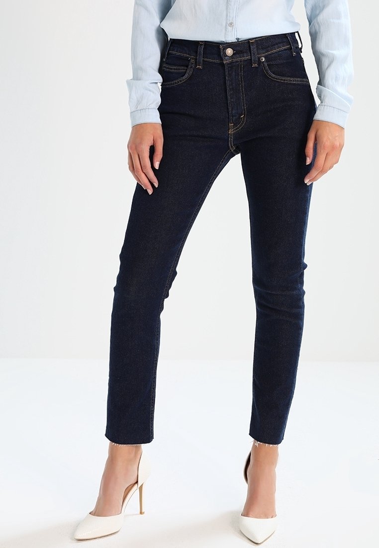 Jean skinny bleu foncé à taille haute, fabriqué en denim. Comprend des passants pour ceinture, des poches avant et un détail de coutures minimaliste.