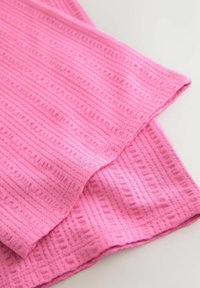 Zbliżenie na złożoną różową tkaninę o fakturze z wypukłymi, prostokątnymi i liniowymi wzorami na białej powierzchni.