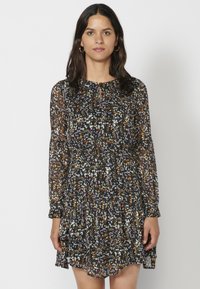 Schwarzes Langarm-Kleid mit Blumenmuster und gestuftem Rock, das ein überall vorhandenes Muster mit weißen, orangen und grünen Akzenten aufweist und aus einem transparenten Stoff gefertigt ist.