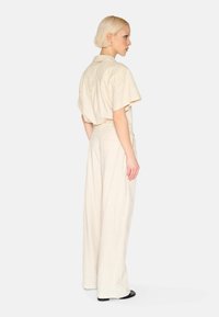 Beige linne tvådelad outfit med en kortärmad topp med krage och vida byxor. Texturen verkar lätt och andas.