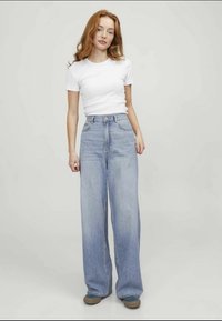 Lyseblå stretchbukser med høy midje, store lommer og en falmet finish, sammen med en tettsittende hvit t-skjorte og brune sneakers.