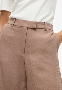 Pantaloni in misto lino marroni con una texture liscia, design sartoriale, passanti per cintura lungo la vita e tasche laterali.