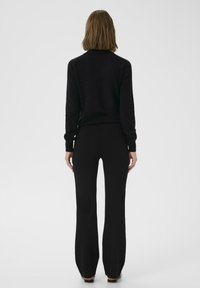 Maglione nero a maglia con collo alto e maniche lunghe, abbinato a pantaloni neri svasati. Texture liscia, silhouette aderente e design minimalista.
