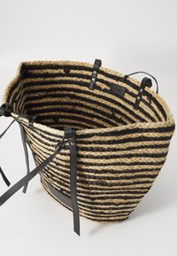 Round woven straw bag with black and natural striped pattern. Features black leather handles and accents, showing textured craftsmanship.