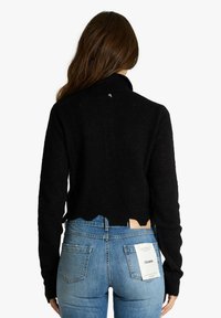Maglione nero e strutturato con collo alto e orlo irregolare. Abbinalo a jeans azzurri chiari con tasche posteriori ed etichetta del marchio.