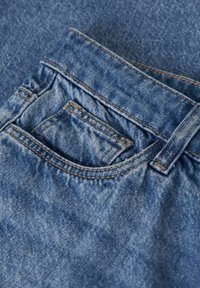 Denim tkanina v svetlo modri barvi, ki vključuje majhno žep in zanke za pas. Končana je z rahlo obrabljenim videzom in vidnimi šivi.