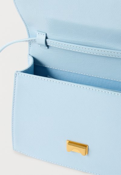 Ανοιχτό μπλε δερμάτινη τσάντα χειρός με χρυσό ορθογώνιο κλειδί, ανοιχτή για να φαίνεται η εσωτερική επένδυση και η θηλιά του ιμάντα μέσα στη φλίπα.