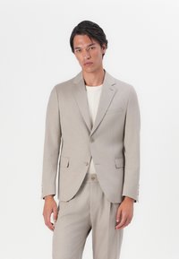 Beige tailored suit made of lightweight fabric, featuring a single-breasted jacket with notch lapels and two front pockets, paired with matching trousers.