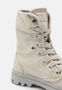High-top canvas boot in light beige, featuring a textured surface, lace-up front, and a gray rubber sole with a patterned tread.