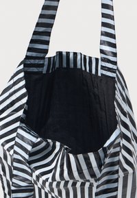 Svart og lyseblå stripete totebag med robuste håndtak, som har et romslig svart interiør og en myk, teksturert overflate.