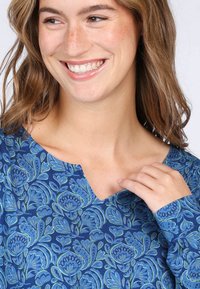 Blaue gemusterte Bluse mit floralem Design in Grüntönen und Blautönen, mit einem dezenten V-Ausschnitt und langen Ärmeln. Weiche Stofftextur.