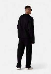 Ensemble de sweatshirt et pantalon noir, fabriqué en tissu doux. Coupe ample, texture subtile, avec un design épuré et des baskets blanches en contraste.