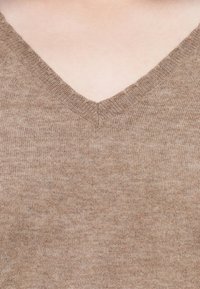 Maglione a V in morbido tessuto a maglia beige, con una texture fine e un motivo sottile, dotato di scollatura a costine.