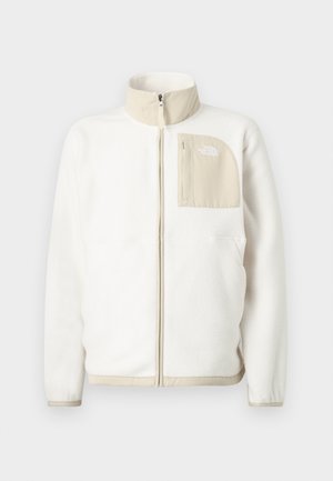 Bílá fleecová bunda s béžovou zipovou kapsou, vysokým límcem a decentním logem na hrudi. Hladká textura s moderním střihem.