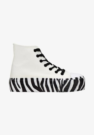 High-Top Sneaker mit einem weißen Canvas-Obermaterial, schwarzen Schnürsenkeln und einer Gummi-Außensohle in Zebra-Streifen schwarz-weiß. Mit einer abgerundeten Zehenpartie.