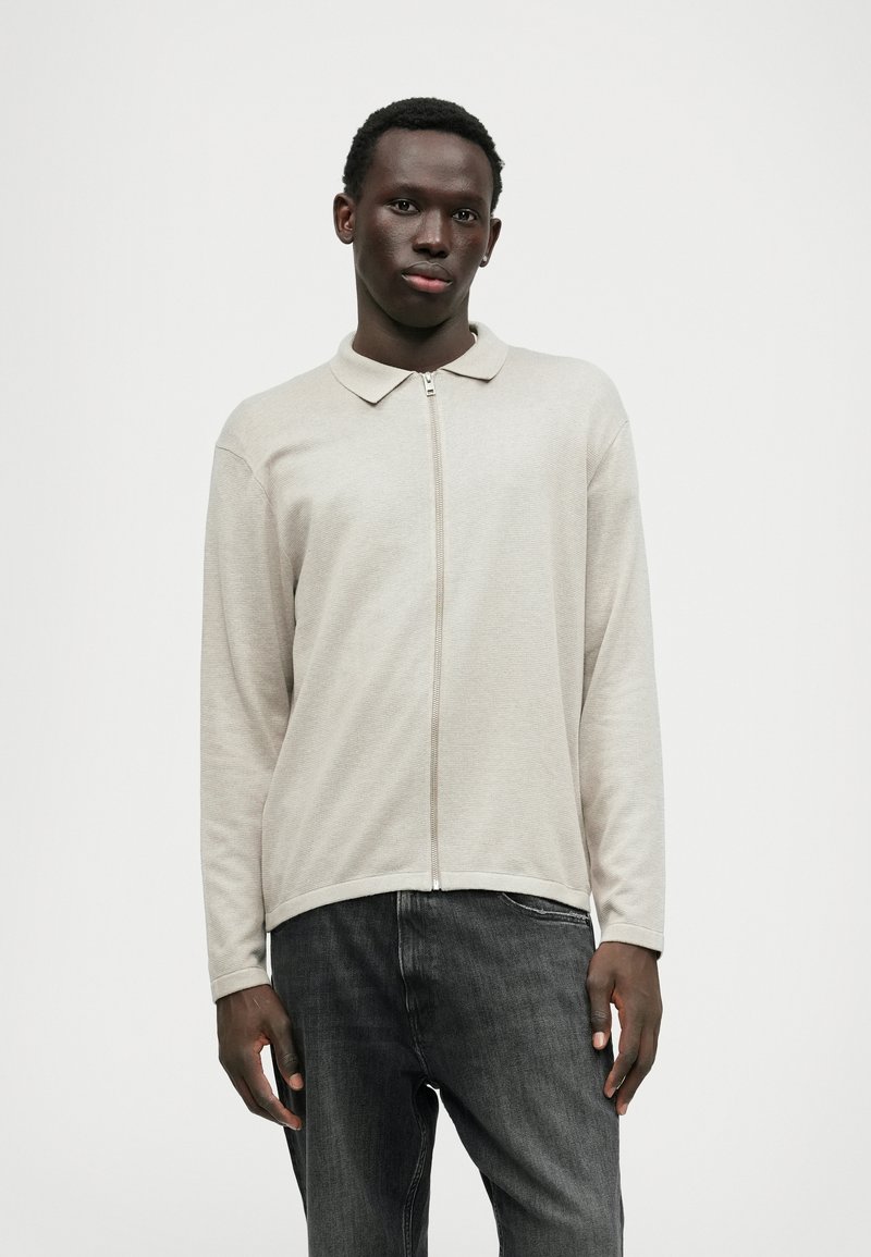 Beige lynlås langærmet top med en blød tekstur, krave og afrundet kant, parret med mørke denim jeans. Enkel, afslappet design.