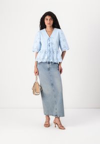 Top azzurro chiaro a maniche corte con dettagli a occhio e vita con coulisse, abbinato a una lunga gonna in denim aderente e una borsa beige.