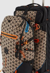 Due zaini, uno più grande e uno più piccolo, presentano un motivo geometrico beige e nero con accenti arancioni e blu. Cinghie regolabili visibili.