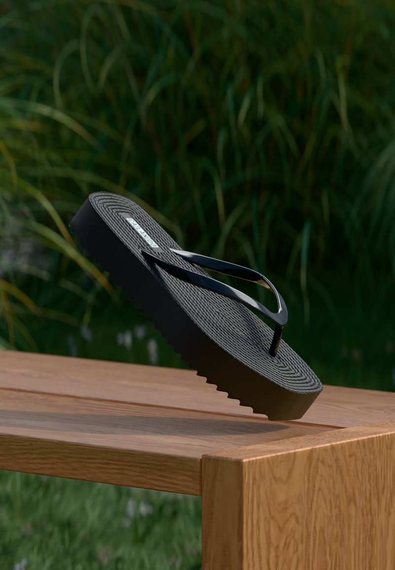 Tongs à plateforme noire avec semelle texturée, équilibrées sur le bord d'un banc en bois en plein air, avec en arrière-plan un feuillage vert flou.