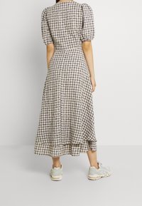 Maxiklänning med puffärmar, i beige och marinblå rutigt mönster, flödande tyg, nästan ankellång, kombinerad med ljusgröna sneakers.