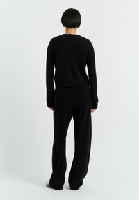 Zwarte gebreide trui gecombineerd met een bijpassende losse zwarte broek. De stof lijkt zacht met een geribbeld patroon.