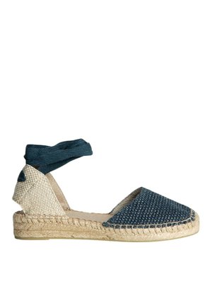 Espadrille de lona azul con textura tejida, suela de yute y una correa de tela en el tobillo. Presenta una punta redondeada y paneles laterales beige.