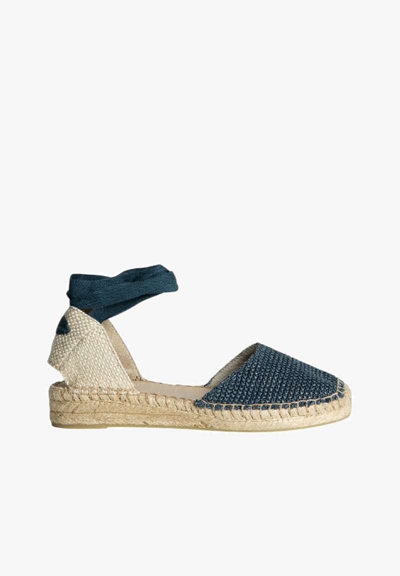 Espadrille de lona azul con textura tejida, suela de yute y una correa de tela en el tobillo. Presenta una punta redondeada y paneles laterales beige.