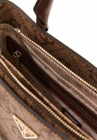 Intérieur de sac à main marron à motifs avec plusieurs compartiments zippés. Dispose d'une doublure en tissu lisse et d'une petite poche sécurisée par un bouton-pression.