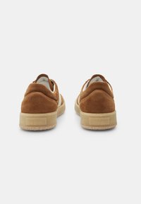 Sneaker in suede marrone con tacco rialzato e suole in gomma color crema a contrasto. Progettate con bordi arrotondati e accenti posteriori minimalisti.