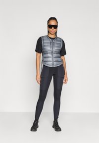 Lengvas pilkas pūkuotas liemuo su užtrauktuku, derinamas su juoda marškinėliais ir juodomis sportinėmis leginsais su tekstūruotais intarpais. Pridedamos juodos sportbačiai.