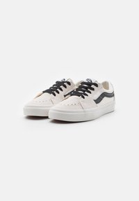 Ein Paar cremefarbene Vans-Sneaker mit schwarzen Schnürsenkeln und seitlichem Streifen auf weißem Hintergrund.