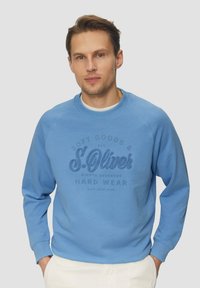 Felpa azzurro chiaro con polsi e scollatura a coste, caratterizzata da una stampa logo testurizzata in blu scuro. Tessuto felpato morbido, vestibilità casual.